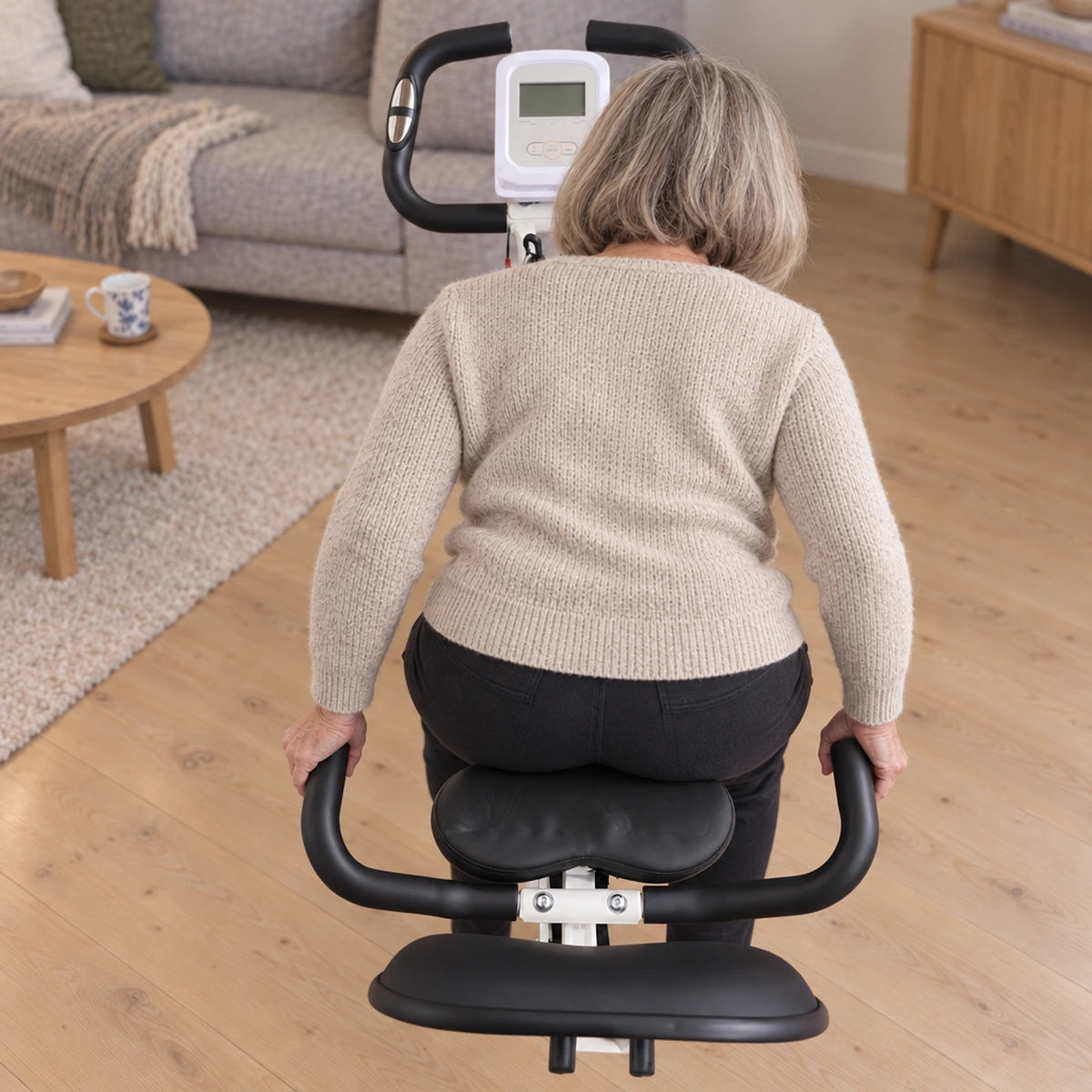 Kvinde holder i håndtagene på hver side af sædet, mens hun sætter sig på AVA foldbar motionscykel